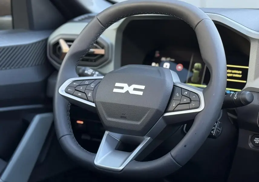 Gros plan sur le volant noir du Dacia Bigster 2026 avec commandes intégrées et tableau de bord numérique en arrière-plan.