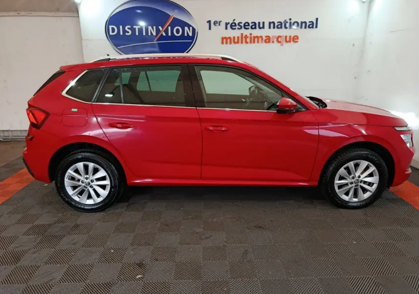 Vue de profil côté droit d'un Skoda Kamiq rouge 2024 avec rails de toit noirs dans un showroom.