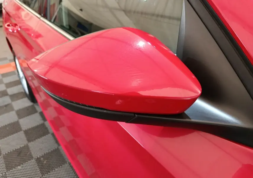 Gros plan sur le rétroviseur côté gauche rouge vif du Skoda Kamiq 2024 avec carrosserie et vitre partiellement visibles.