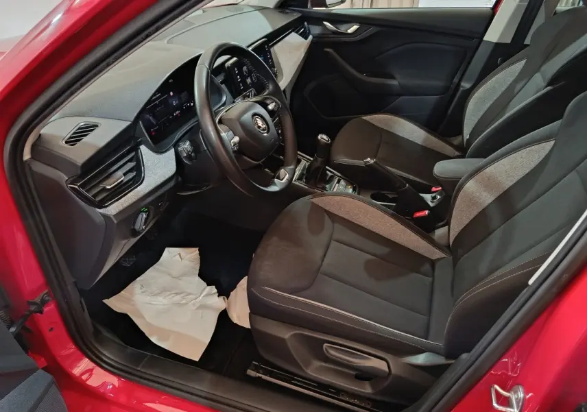 Vue intérieure côté conducteur du Skoda Kamiq rouge 2024, volant cuir multifonctions et sièges tissu bicolores.