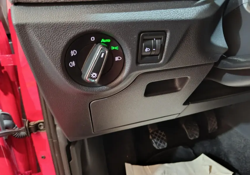 Détail du panneau de commande des phares à gauche du volant d’un Skoda Kamiq rouge 2024, avec réglage automatique activé.