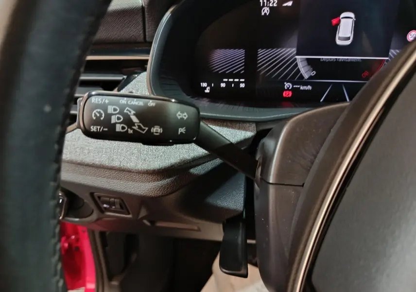 Gros plan sur le commodo gauche du volant cuir d’un Skoda Kamiq rouge, avec tableau de bord numérique en arrière-plan.