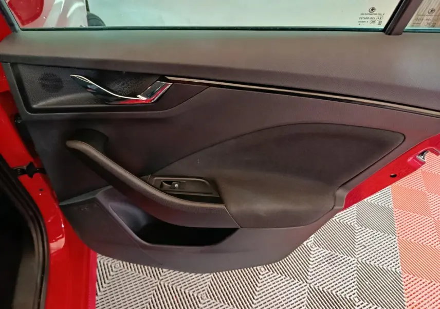 Vue intérieure côté gauche de la porte avant rouge du Skoda Kamiq 2024 avec poignée chromée et commande de vitre électrique.
