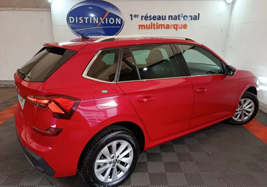 Vue 3/4 arrière droite d’un Skoda Kamiq rouge 2024 avec barres de toit noires et vitres teintées.