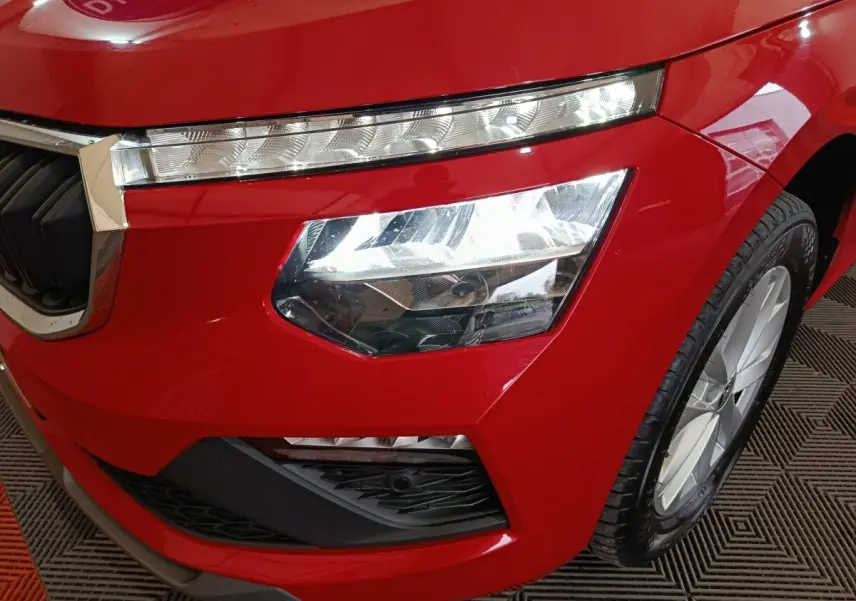 Gros plan sur l'avant droit rouge vif du Skoda Kamiq 2024, mettant en valeur le phare LED et la calandre chromée.