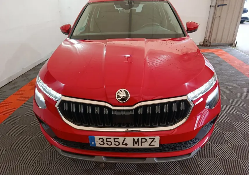 Vue avant d'un Skoda Kamiq rouge 2024 avec calandre noire et phares LED allumés dans un garage.