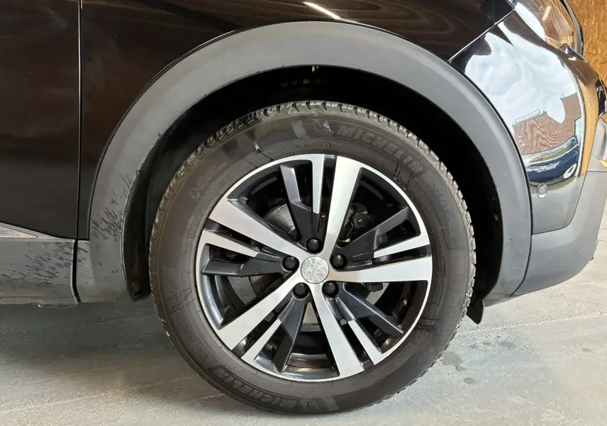 Gros plan sur la roue avant droite du Peugeot 3008 noir, mettant en valeur la jante alliage bicolore et le pneu Michelin.