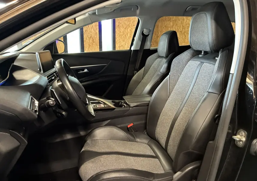 Vue intérieure côté conducteur du Peugeot 3008 noir, montrant les sièges tissu et cuir ainsi que le tableau de bord moderne.