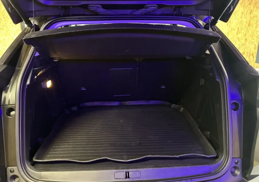 Coffre ouvert vu de l'arrière d'un Peugeot 3008 noir 2020, avec tapis de coffre en caoutchouc et éclairage intérieur allumé.