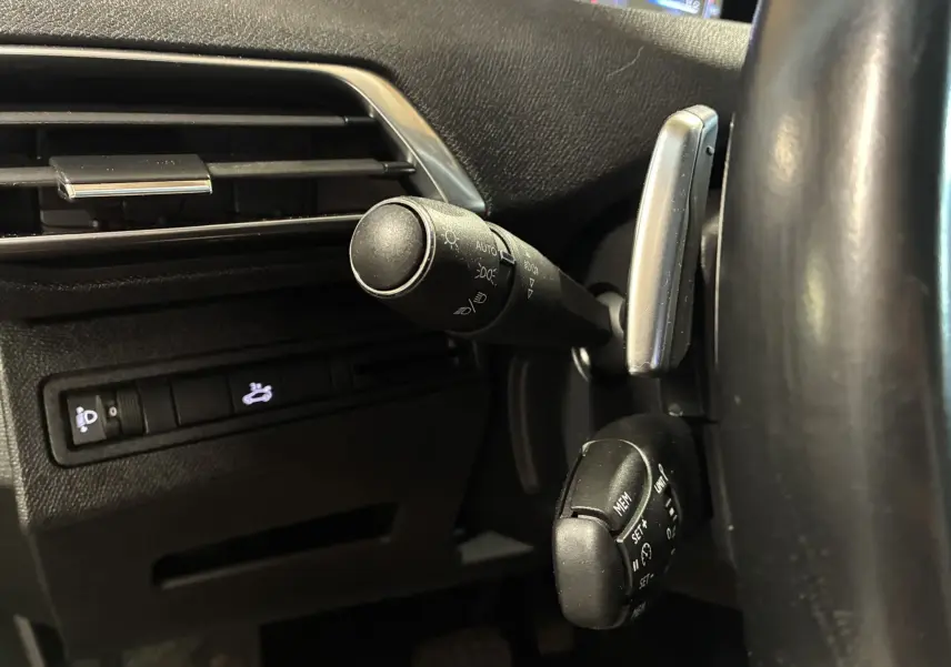 Gros plan sur les commandes au volant côté gauche du Peugeot 3008 noir, mettant en valeur les leviers de clignotants et régulateur de vitesse.