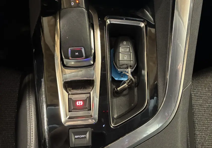 Vue en plongée sur la console centrale noire du Peugeot 3008 1.5 BlueHDi 130, avec levier de vitesse automatique et clé posée.