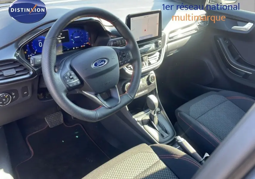 Vue intérieure côté conducteur du Ford Puma 2023, volant cuir perforé, tableau de bord numérique et sellerie tissu noir avec surpiqûres rouges.