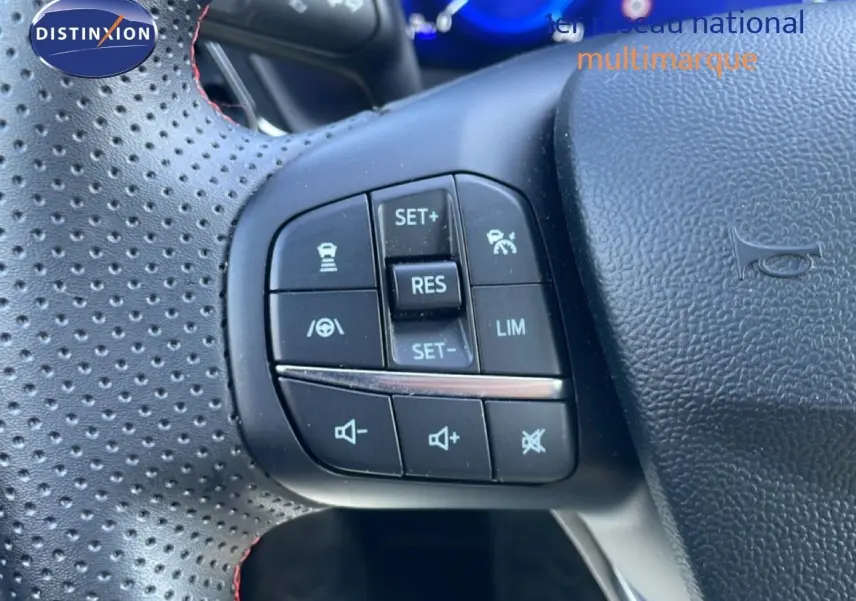 Gros plan sur les commandes de régulateur et volume au volant perforé noir du Ford Puma gris Solar Metal 2023.