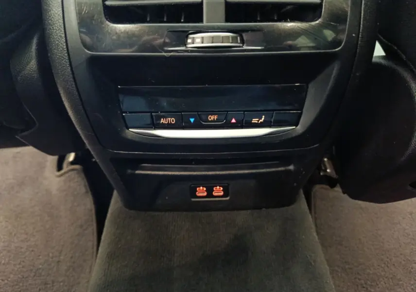 Détail de la console arrière noire du BMW X3 xDrive30e 2020 avec commandes climatisation et prises USB éclairées rouges.
