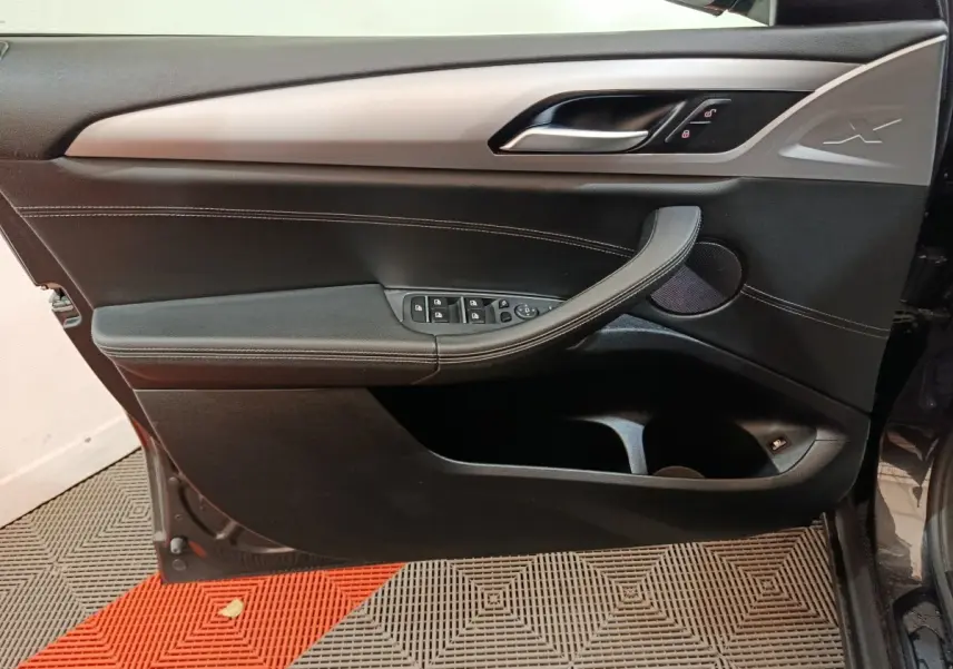 Vue intérieure côté gauche de la porte avant BMW X3 xDrive30e gris foncé avec commandes de vitres et logo X embossé.