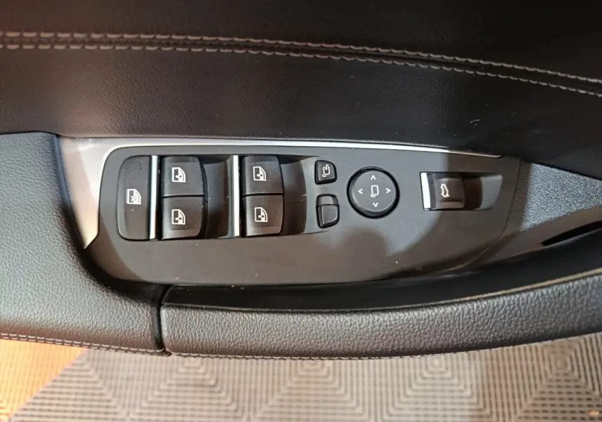 Gros plan sur les commandes de lève-vitres et rétroviseurs sur la porte côté conducteur du BMW X3 gris foncé.