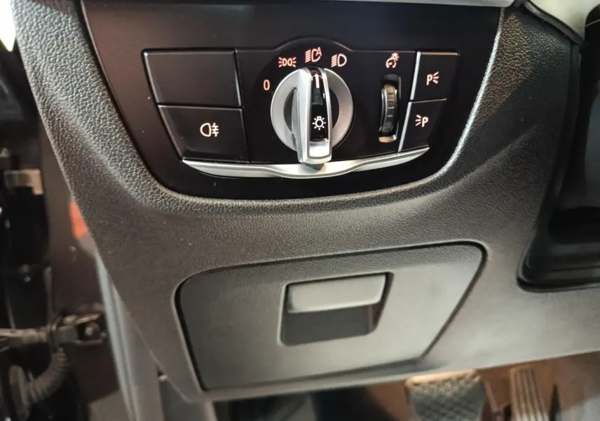 Gros plan sur le panneau de commande des phares et feux, intérieur noir du BMW X3 xDrive30e gris foncé.