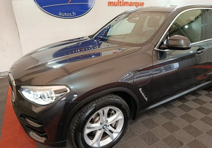 Vue 3/4 avant gauche d’un BMW X3 xDrive30e gris foncé avec jantes alliage et feux LED allumés.