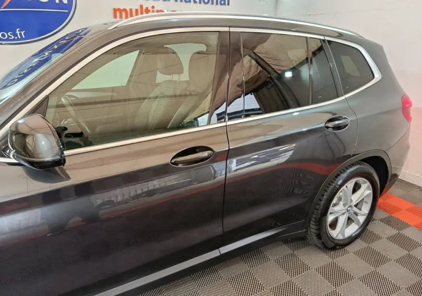 Vue latérale côté gauche d’un BMW X3 gris foncé avec jantes alliage et rails de toit chromés visibles.