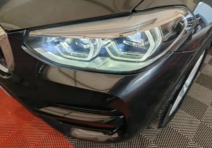 Gros plan sur le phare avant droit du BMW X3 xDrive30e gris foncé, mettant en valeur les détails LED et la carrosserie brillante.