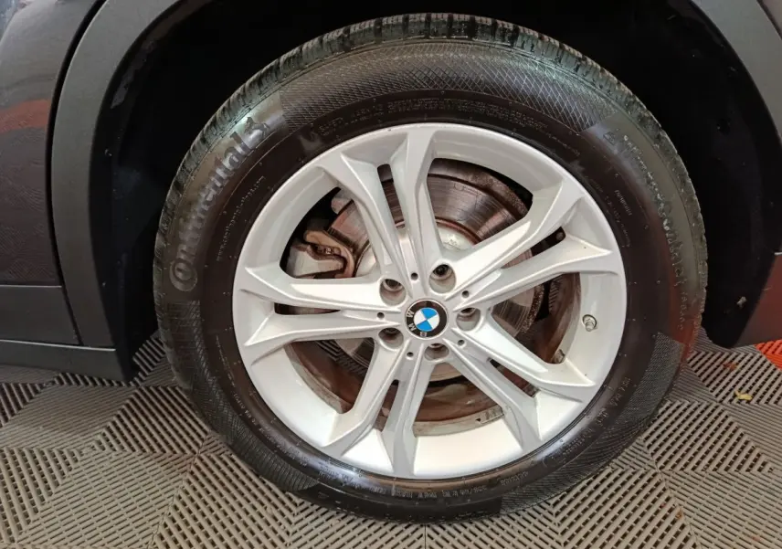Gros plan sur la roue avant gauche avec jante argentée et logo BMW sur un BMW X3 gris foncé hybride rechargeable.