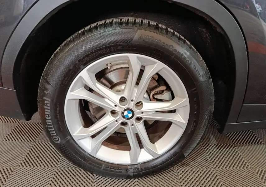 Gros plan sur la roue avant droite d'un BMW X3 gris foncé, avec jante alliage argentée et logo BMW central.