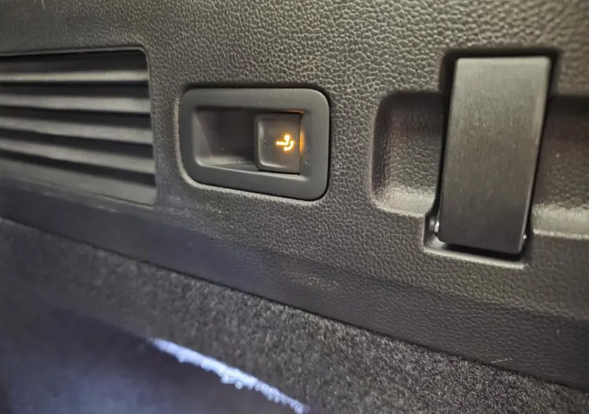 Gros plan sur le bouton d'abattement électrique des sièges arrière dans le coffre du Volkswagen Arteon gris Shooting Brake.