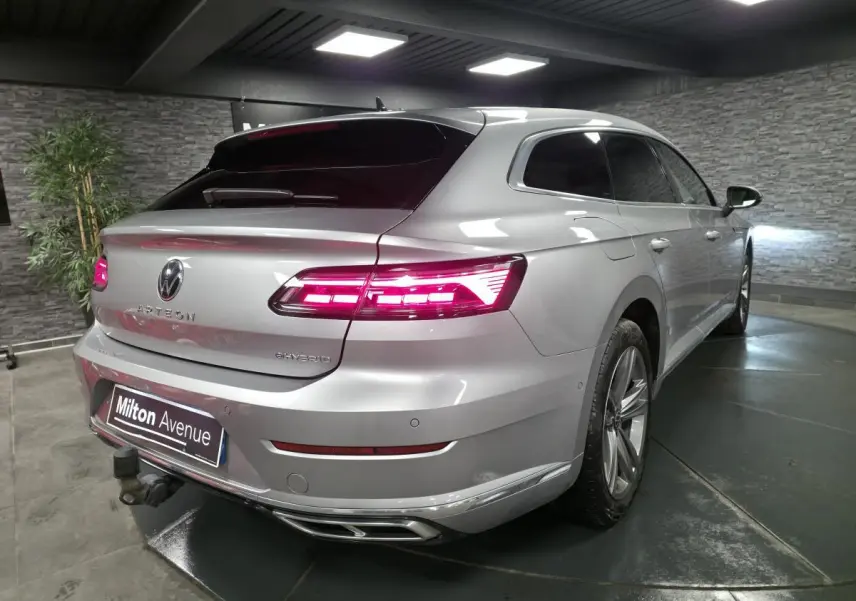 Vue 3/4 arrière droite d'une Volkswagen Arteon Shooting Brake gris métallisé avec feux arrière LED allumés et attelage rabattable.
