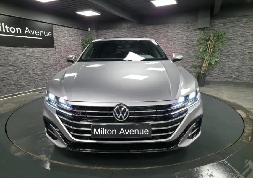 Vue avant d'une Volkswagen Arteon Shooting Brake gris métallisé avec calandre R-Line et phares LED allumés en showroom.