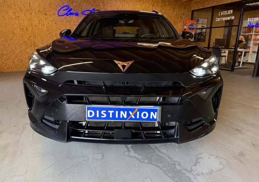 Vue frontale d'un CUPRA Formentor noir 2025 avec phares allumés et logo cuivré sur calandre sportive.