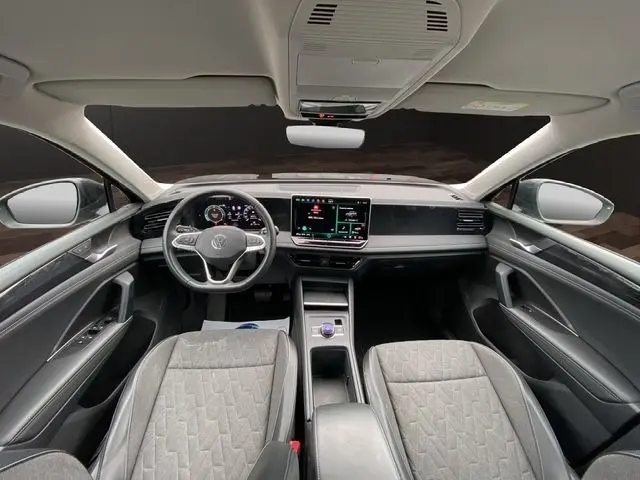 Vue intérieure avant du Volkswagen Tiguan 2024 noir, tableau de bord moderne avec écran tactile central et volant multifonctions cuir.