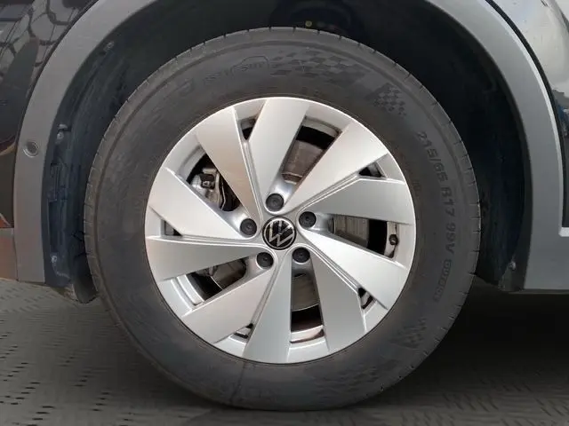 Gros plan sur la roue avant droite noire d’un Volkswagen Tiguan 2.0 TDI 150 DSG7 avec jante argentée à design moderne.