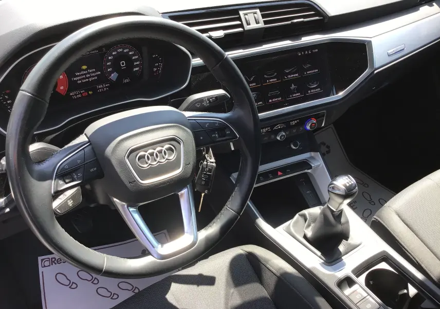 Vue intérieure de l'Audi Q3 Sportback 2024, tableau de bord noir avec volant cuir et levier de vitesse manuel.