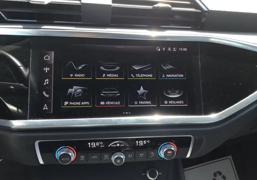 Vue rapprochée de l’écran tactile central et de la console de climatisation du tableau de bord d’un Audi Q3 Sportback gris clair métal.