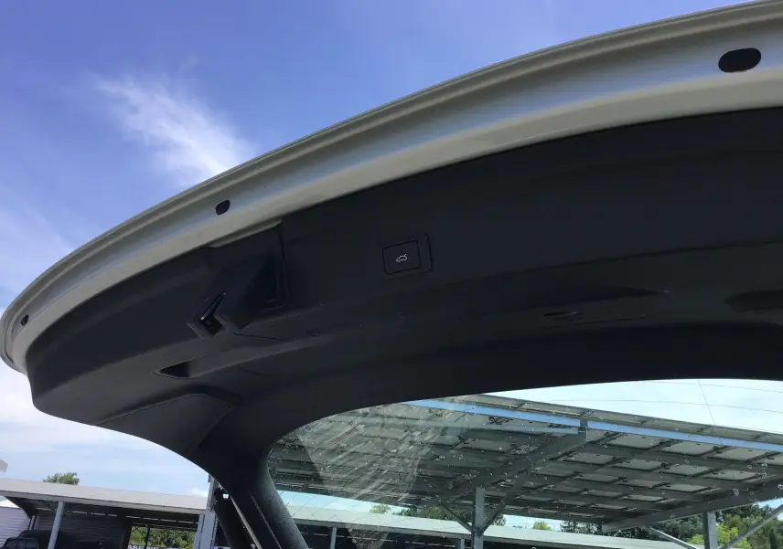 Vue en contre-plongée de la porte de coffre ouverte d’un Audi Q3 Sportback gris clair métal sous un ciel bleu.