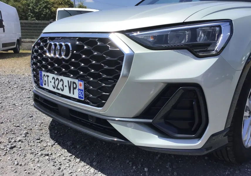 Vue de face côté droit d’un Audi Q3 Sportback gris clair métal, mettant en valeur la calandre hexagonale noire et les phares LED.