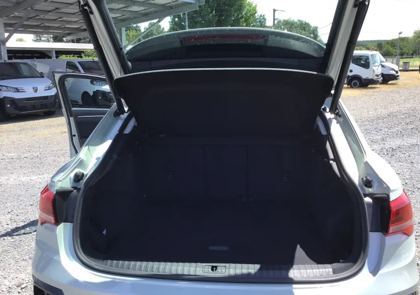 Coffre ouvert vu de l'arrière d'un Audi Q3 Sportback gris clair métal 2024, avec hayon relevé et intérieur spacieux.