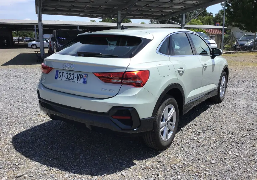 Audi Q3 Sportback gris clair métal vue 3/4 arrière droit, avec feux arrière allumés et jantes 17 pouces.