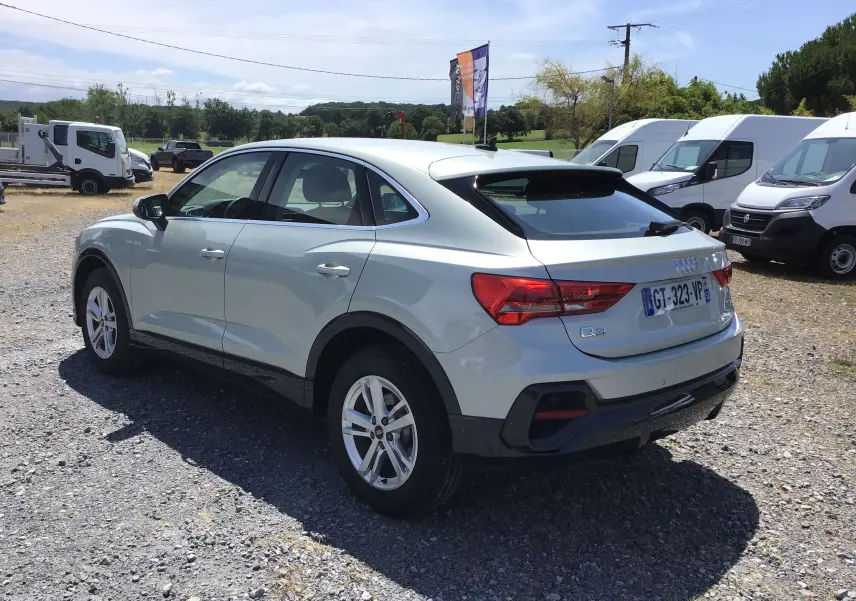 Audi Q3 Sportback gris clair métal vue 3/4 arrière droit, soulignant ses lignes fluides et ses feux arrière distinctifs.