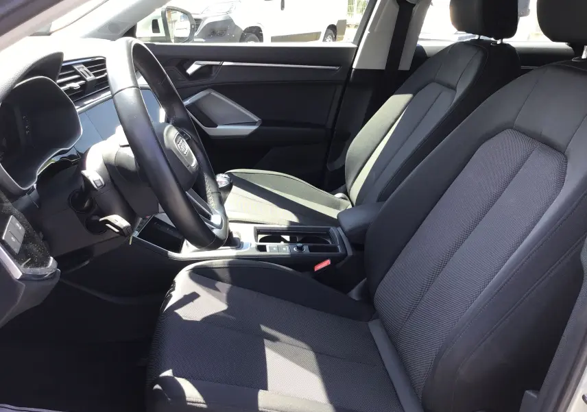 Vue intérieure côté conducteur de l'Audi Q3 Sportback 35 2.0 TDI 150 Design avec sièges tissu noirs et tableau de bord moderne.
