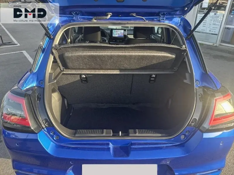 Coffre ouvert vu de l'arrière d'une Suzuki Swift 1.2 Hybrid bleu Frontier Pearl Metal, intérieur de coffre vide et tablette cache-bagages.