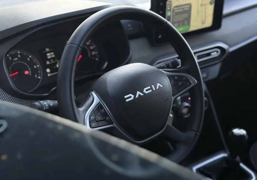 Vue rapprochée du volant noir du Dacia Jogger 2025 avec tableau de bord et écran tactile GPS en arrière-plan.