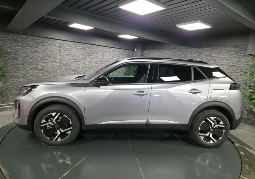 Vue latérale droite d'un Peugeot 2008 gris métallisé avec jantes bi-ton et toit noir en intérieur showroom.