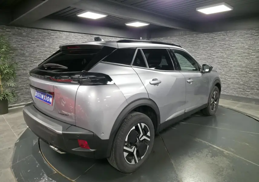 Vue 3/4 arrière droite d'un Peugeot 2008 gris métallisé avec jantes alliage bi-ton et toit noir en intérieur showroom.