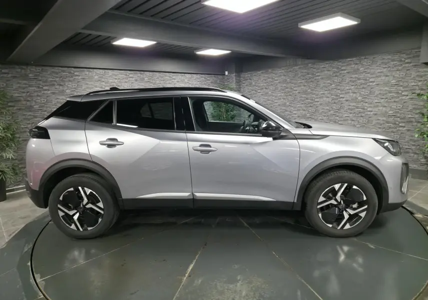 Peugeot 2008 gris en profil droit dans un showroom, avec jantes alliage bi-ton et vitres teintées.