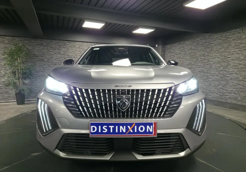 Vue avant du Peugeot 2008 gris 2025 avec calandre verticale chromée et feux LED allumés dans un showroom.
