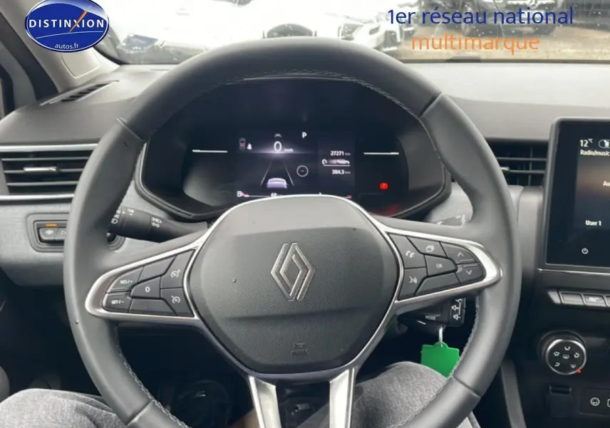 Vue intérieure centrée sur le volant multifonction noir d'une Renault Clio V blanche, avec tableau de bord digital et écran tactile visible.