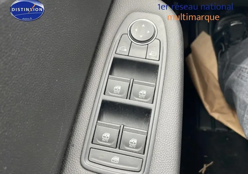 Gros plan sur les commandes de lève-vitres et rétroviseurs côté conducteur d'une Renault Clio V blanche, intérieur noir.