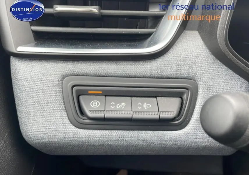 Gros plan sur les commandes d’éclairage et verrouillage sur tableau de bord gris de la Renault Clio V blanche.