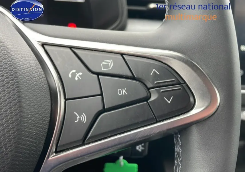Gros plan sur les commandes multifonctions noires du volant de la Renault Clio V blanche, avec finition argentée.